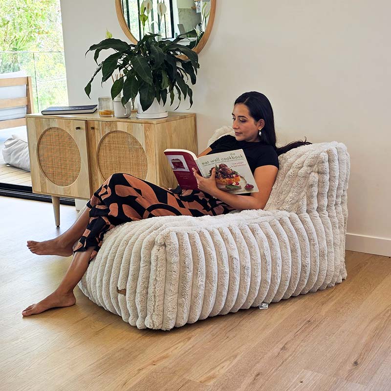 Brooklyn Luxe Lounger Foam Filled Bean Bag in Corduroy Faux Fur by Mooi Living in a living room, woman seated comfortably and reading.