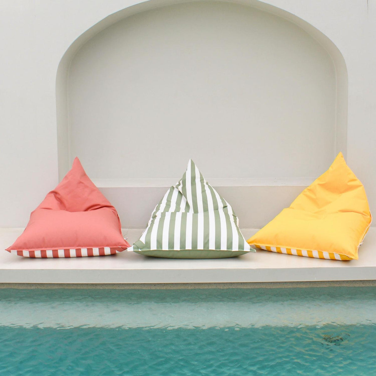 Mooi Living reversible triangle outdoor bean bags in blush, sage green stripe and yellow displayed together beside a pool, MOREVSTRIBB-YEL