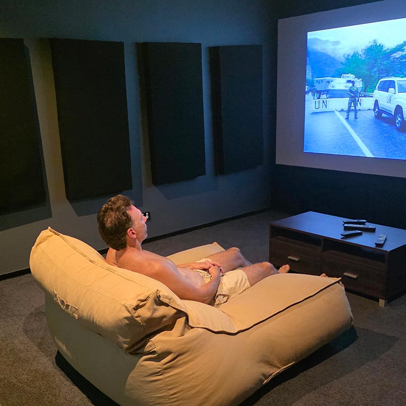 Customer pic of the Double Boss Lounger indoor bean bag by Mooi Living in Tan. A man is sitting on the Double Boss watching TV in a dark room with a projector screen displaying a scene.