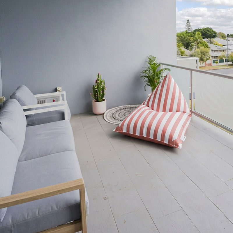Outdoor living space with a Blush Reversible Triangle outdoor bean bag by Mooi Living, gray sofa, and potted plants.