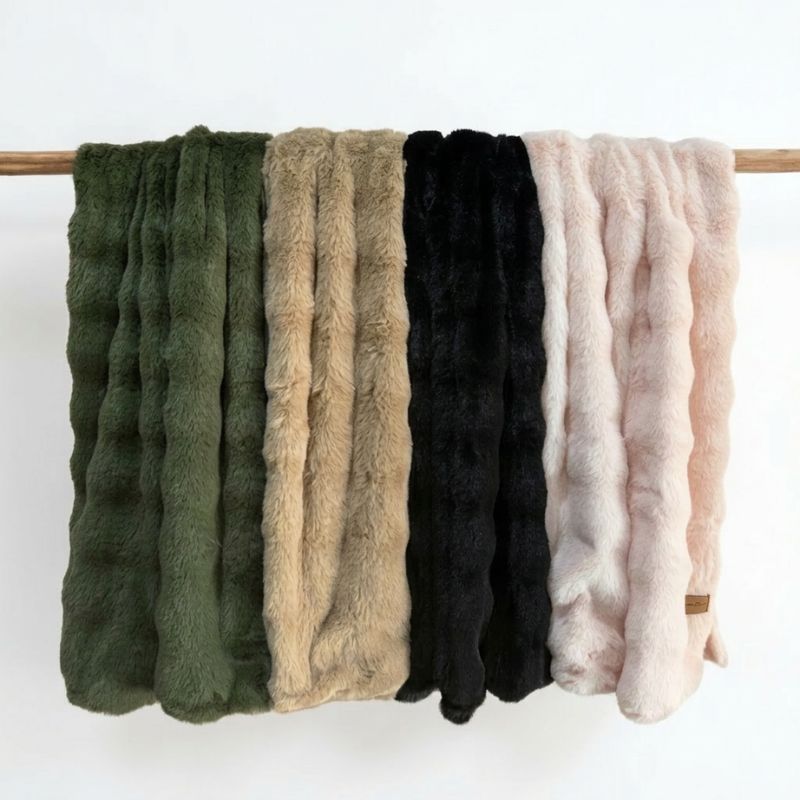 Set of five textured throws in green, beige, black, and pink on a wooden pole