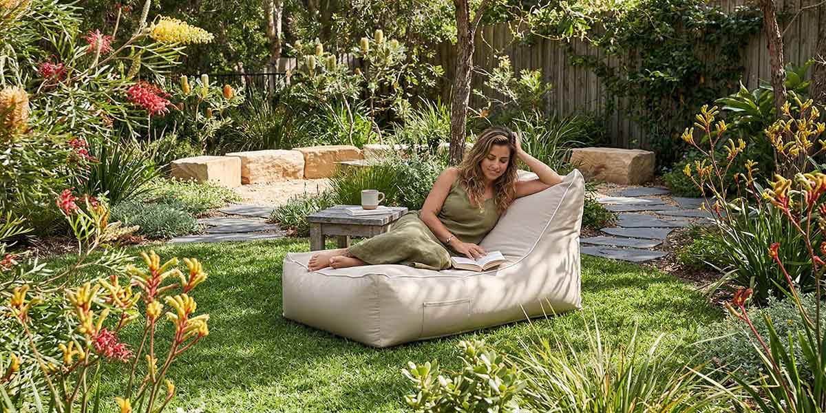 Lush Australian backyard garden with green lawn, native plants and soft landscaping, Lachlan Lounger placed on the grass in dappled sunlight, calm outdoor retreat atmosphere.