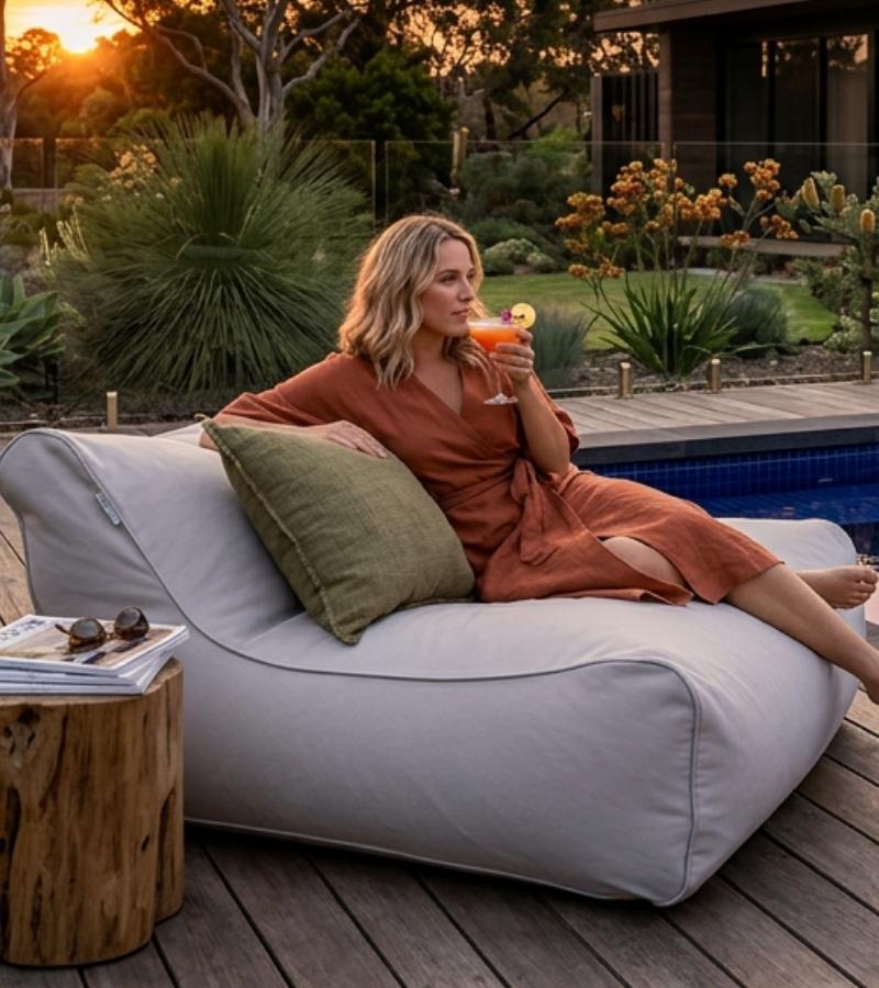 Woman in an orange dress sitting on a Chill Lounger UV Outdoor Bean Bag by Mooi Living by a pool, holding a cocktail.