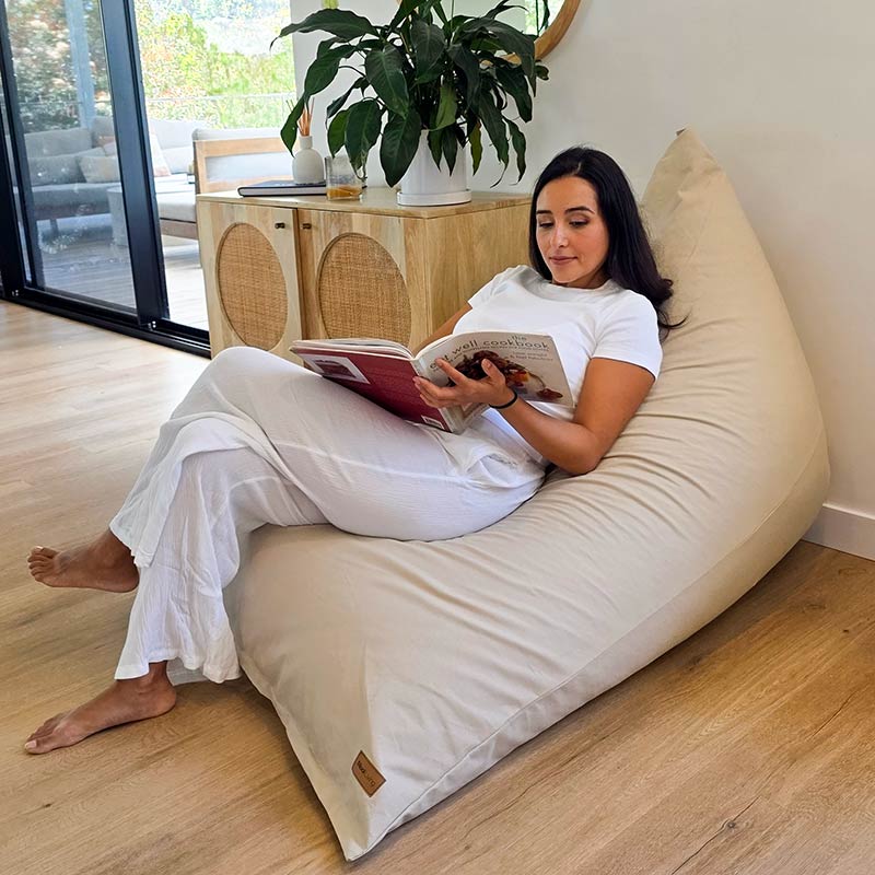 The perfect reading nook - Natural oversized Cotton Canvas Triangle Bean Bag Chair by Mooi Living in a modern living room, lady seated reading a book.