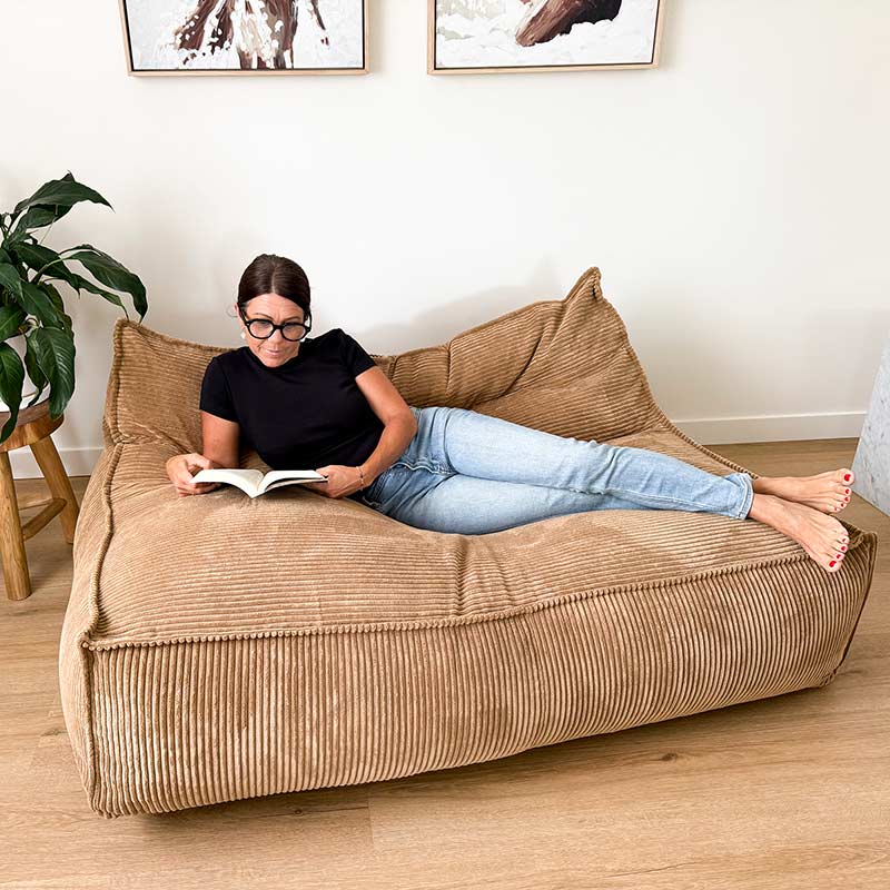 Mooi Double Seater Corduroy Bean Bag Lounger in Caramel by Mooi Living, woman reclining and reading in a living room.