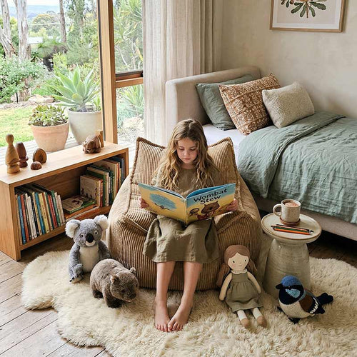 Lifestyle image of the Mini Cord Chair indoor bean bag by Mooi Living in Caramel with a little girl sitting on it while reading a book in a cozy bedroom with toys and plants.