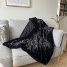 Black faux fur throw blanket draped over a gray sofa in a living room setting.