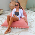 Woman relaxing on the plain blush side of a Mooi Living reversible triangle outdoor bean bag on a tiled patio, MOREVSTRIBB-BLUS