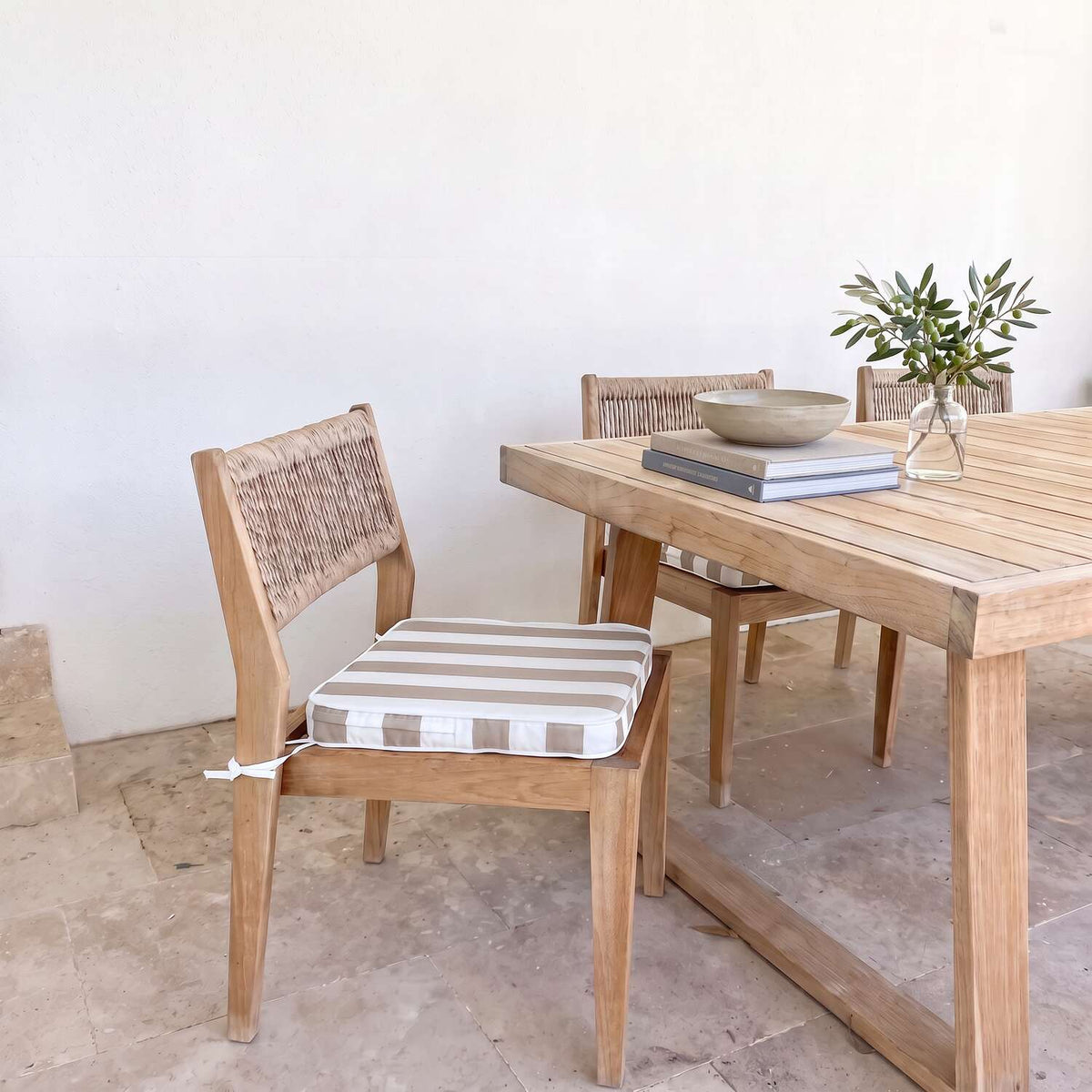 A light oak dining chair with timber matching chairs and a taupe and white striped cushion, shown next to a wooden dining table in a bright, minimalist room.