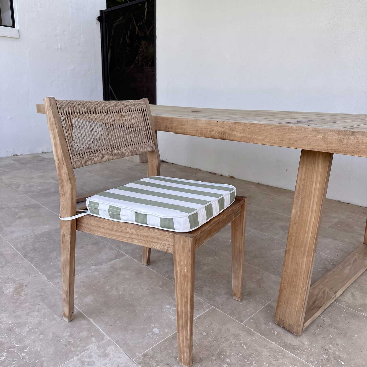 A wooden dining chair with a striped cushion in sage green and white, positioned next to a matching wooden dining table on a stone tiled patio, MOO-STR-GRN-CHPAD
