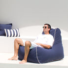 A man sitting and relaxing on a navy Bora Bora bean bag chair with navy and navy whites stripes in the background