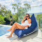 Woman relaxing on the plain navy side of a Mooi Living reversible triangle outdoor bean bag beside a pool, MOREVSTRIBB-NAVY