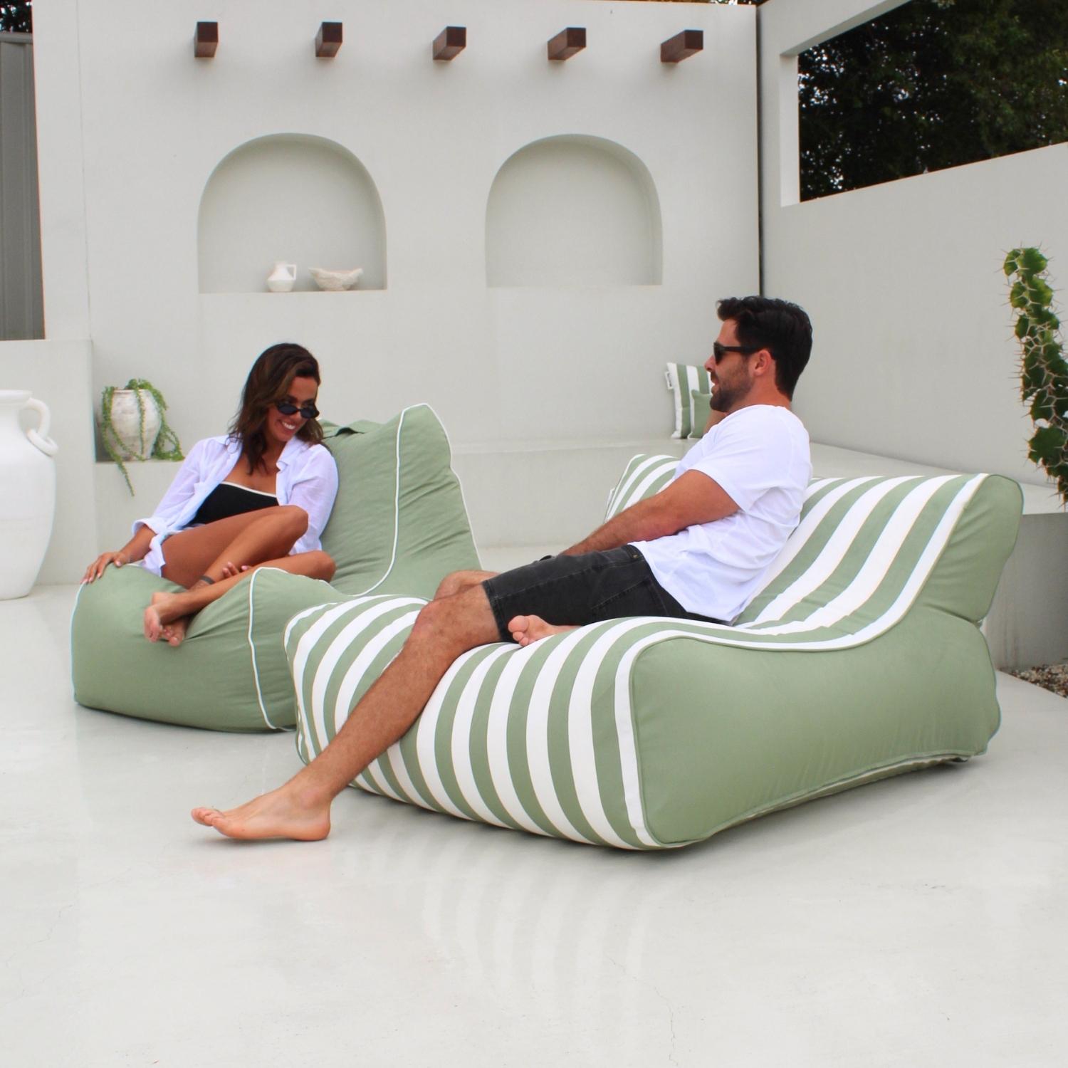 A man and a woman relax on a Bora Bora outdoor bean bag lounge chairs with sage green and white stripes in a modern white patio setting, MOSTRCHILL-BB-GRESTR