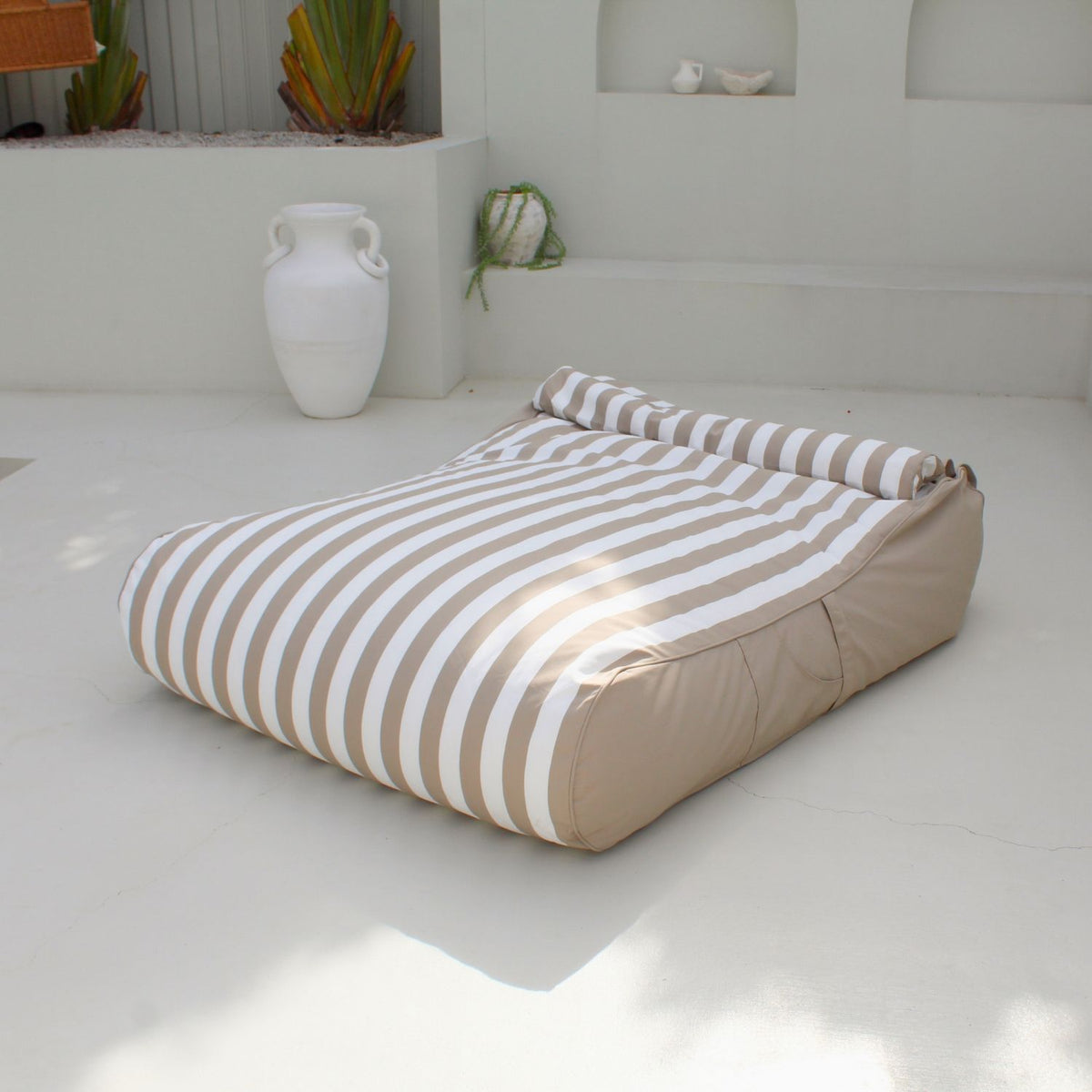 Mooi Living Taupe Stripe Nevaeh double outdoor bean bag sunbed on a white patio, showing its striped surface, plain taupe sides and bolster cushion, MOSTNEVBB-STRI-TAU