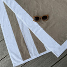 A beige and white striped beach towel laid out on a weathered wooden deck, with a pair of brown sunglasses resting on top.