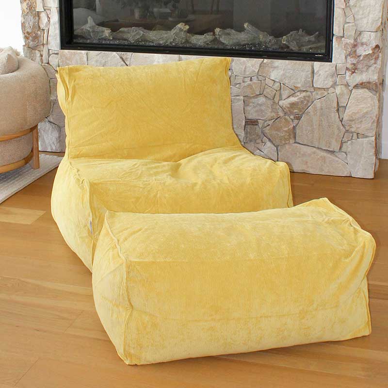 Brooklyn Corduroy bean bag chair in Yellow in a living room with a stone fireplace and television in the background.