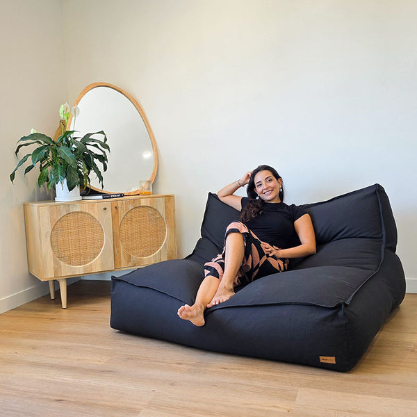 Black Double Boss structured indoor double seater indoor bean bag by Mooi Living in a minimalist interior, lady seated on the bean bag smiling at the camera.