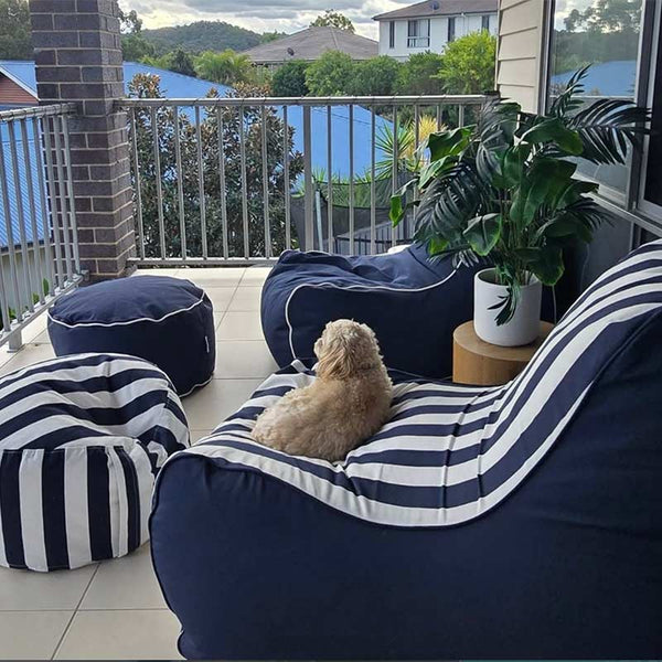 Navy Solid Bora Bean Bag Chair and Navy Stripe Bora Bean Bag with matching ottomans by Mooi Living on a balcony, small fluffy dog sitting on one, customer photo by @felicitykeegan.