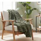 Wooden armchair with a green blanket and white cushion in a room with plants and a table.