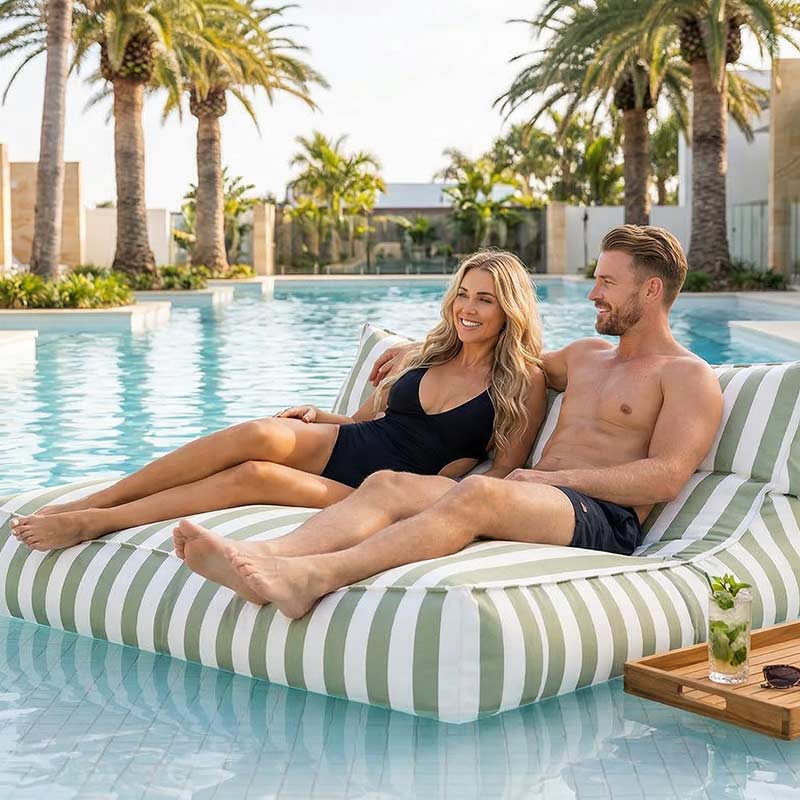 Lifestyle Pic - Luxury resort-style pool in Australia with palm trees, white tiles and clear blue water, two adults relaxing together on a green stripe  Lana double seater bean bag lounger floating on the pool, drinks nearby.