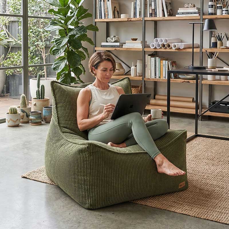 Lifestyle image of Mooi Cord Bean Bag Chair indoor bean bag by Mooi Living in Olive Green with a woman using a tablet on the bean bag chair in a modern living room.