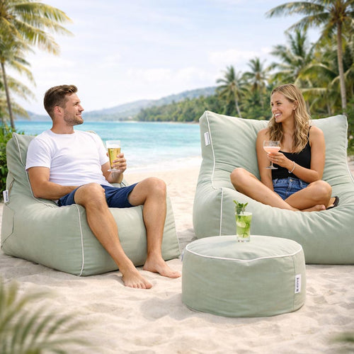 Lifestyle image of the Bora Bora Chair, Chill Lounger UV, and Outdoor Ottoman outdoor bean bag by Mooi Living in Sage Green with two people sitting on the bean bags by the beach with drinks.