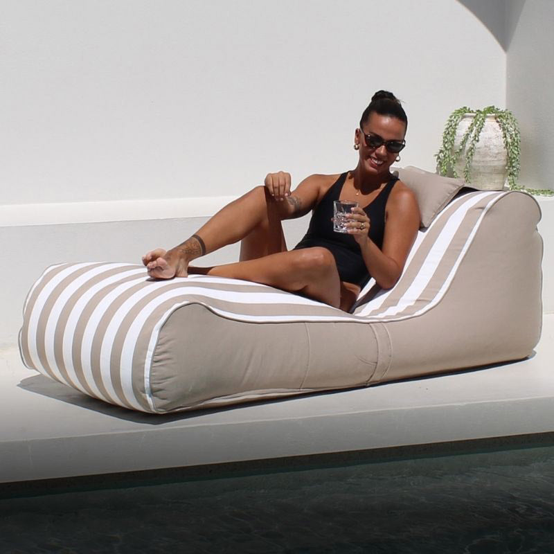 Cojelo Suave Sunlounge in Taupe Stripe outdoor bean bag by Mooi Living, with a woman relaxing on a striped lounge chair by a pool
