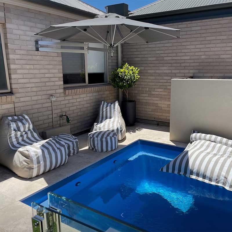 Outdoor patio with pool, Bora Bora Chair Outdoor Bean Bags, Outdoor Ottoman, and Santorini Floating Outdoor Bean Bag by Mooi Living in matching Taupe Stripe, and umbrella