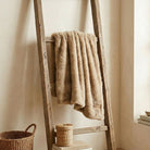 Wooden ladder with a beige throw draped over it against a neutral wall.